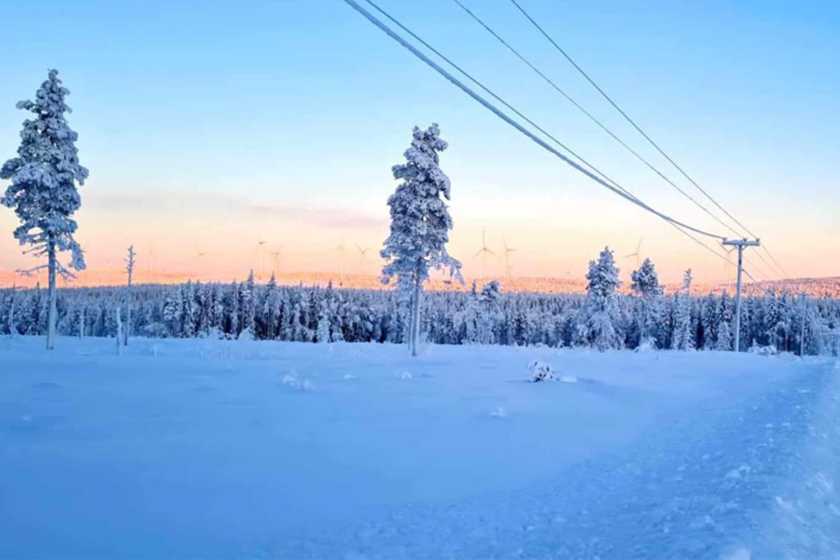 Landskapsbild en solig vinterdag med luftledningar i förgrunden och vindkraftssnurror i bakgrunden