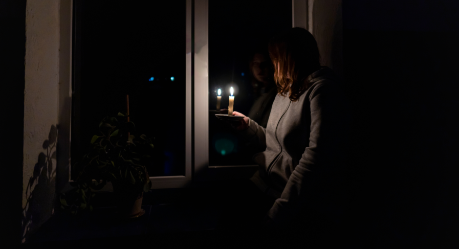 Kvinna tittar ut genom fönstret med ett ljus i handen det är mörkt ute