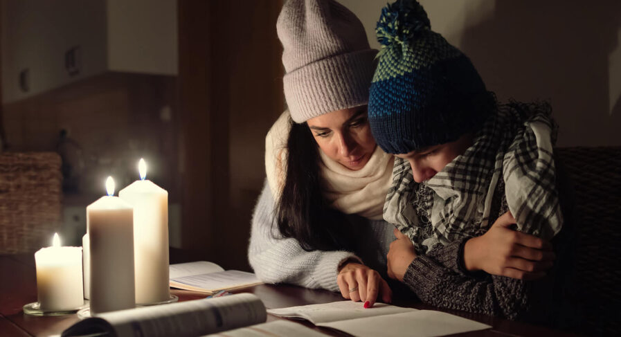 mamma och son sitter i mörkret och läser läxor med mössorna på